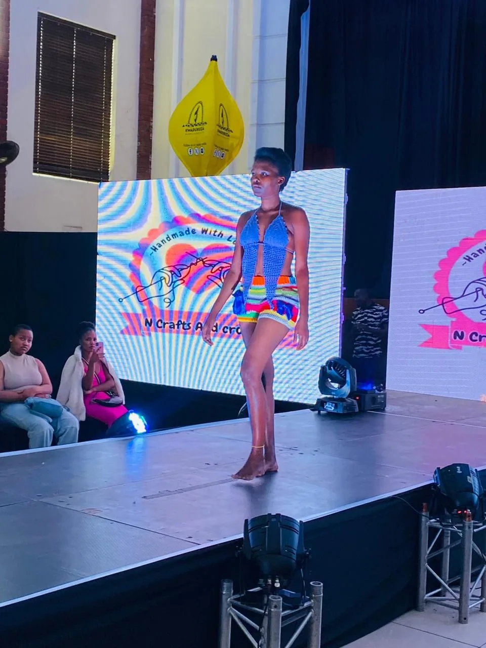 A model on the runway in a bright patterned outfit under the stage lights