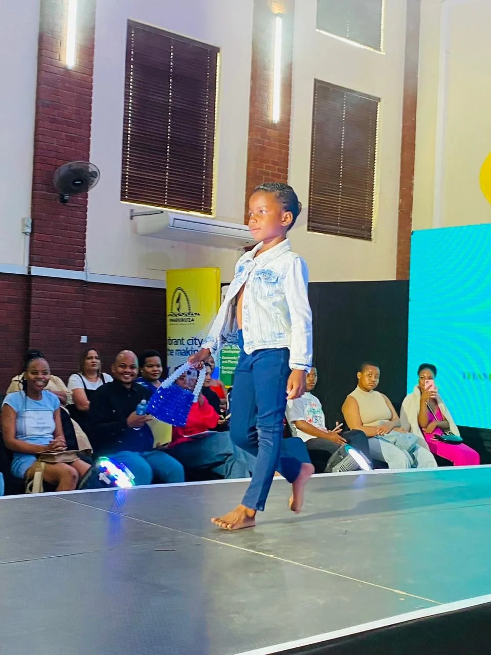 A young child walking the runway to applause from the audience