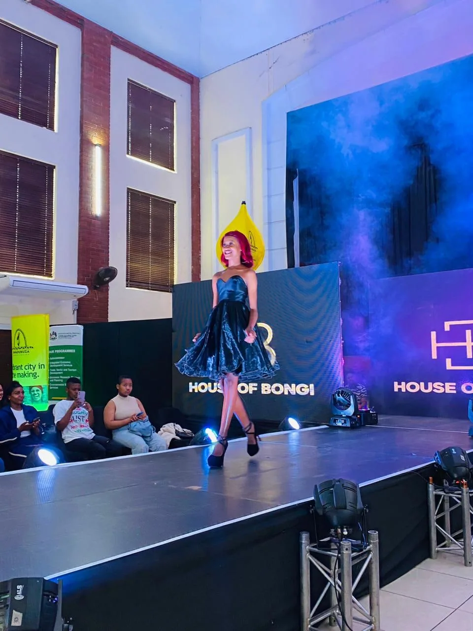 A model presenting a design on the runway under blue stage lighting