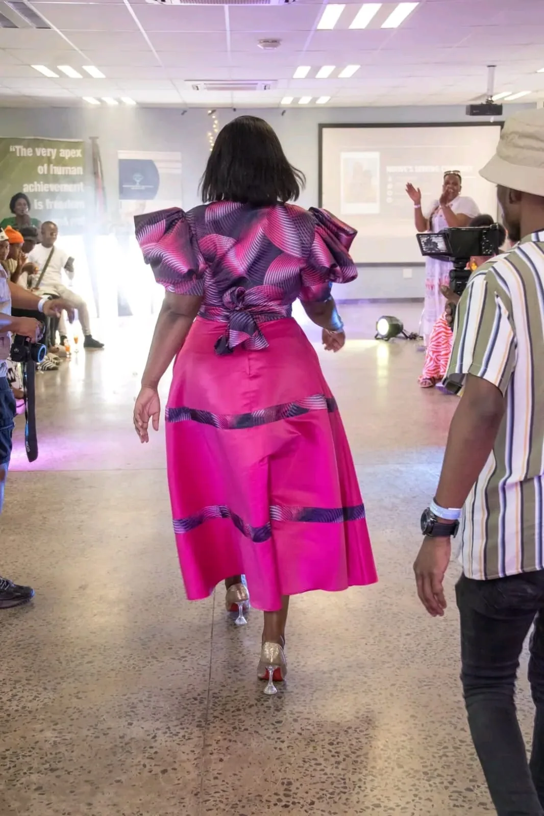 A model in a magenta ruffled dress seen from behind on the runway