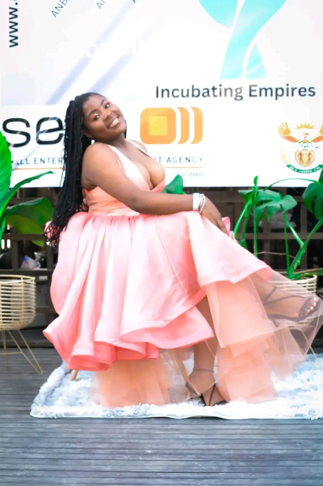 A model in a flowing peach gown in front of the Incubating Empires backdrop